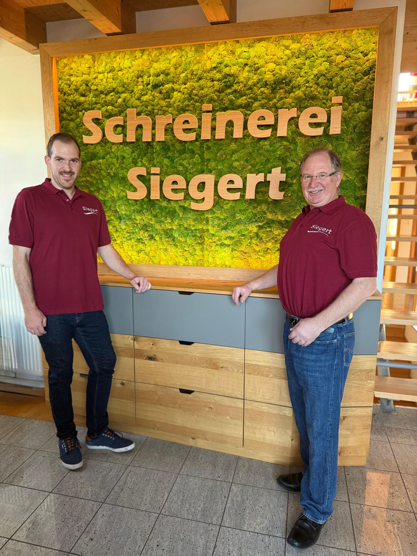 Reinhard und Martin Siegert vor der Moos-Wand mit Schriftzug Schreinerei Siegert